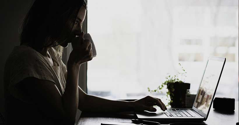 mulher tomando café na frente de um computador.