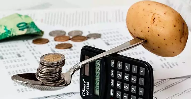 Imagem de uma pilha de moedas em equilibrio com uma batata na outra ponta da balança.
